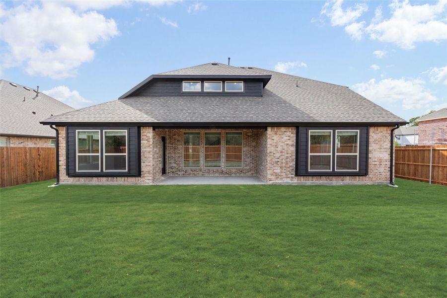 Rear view of single-story brick home with dark trim, covered patio, and large fenced backyard