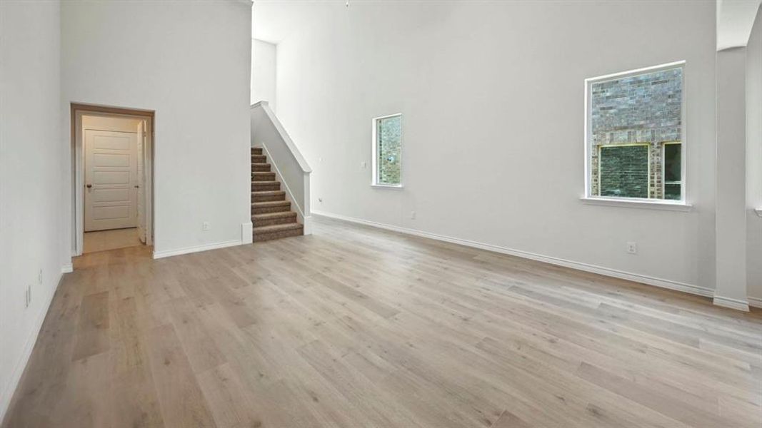 Unfurnished living room with a towering ceiling, light wood-style flooring, and stairway Unfurnished living room with a towering ceiling, light wood-style flooring, and stairway