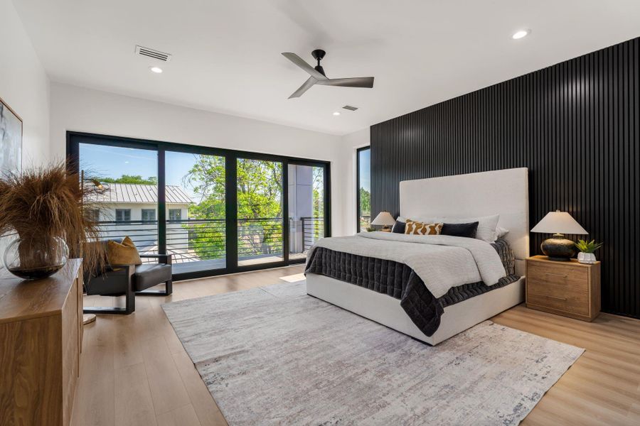 The primary bedroom announces itself — a full wall of vertical black slat cladding anchors the room with a bold architectural moment, while floor-to-ceiling sliding glass panels on the opposite wall open directly to the outdoor balcony.