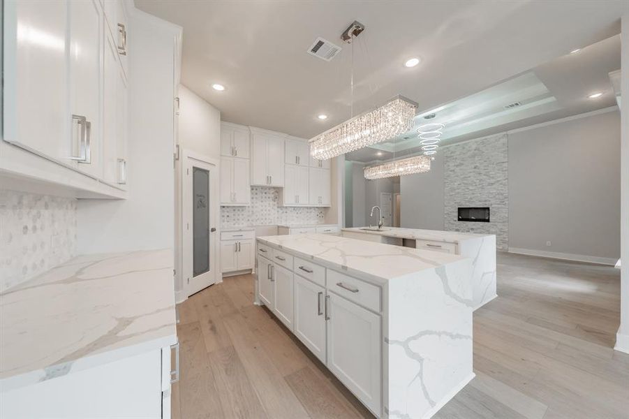 Kitchen featuring light stone counters, white cabinetry, light wood-style flooring, backsplash, and pendant lighting
