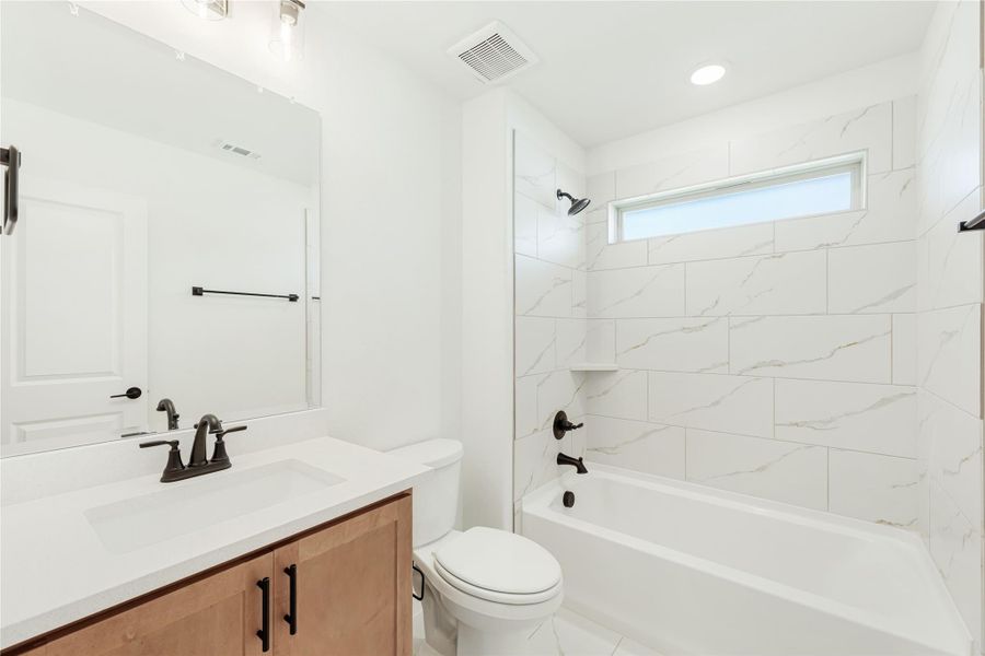 Bathroom with wood vanity, white countertop, and tub-shower combo with marble-look tile surround