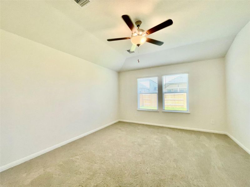 A spacious, naturally illuminated room boasts soft carpeted flooring and an overhead ceiling fan.