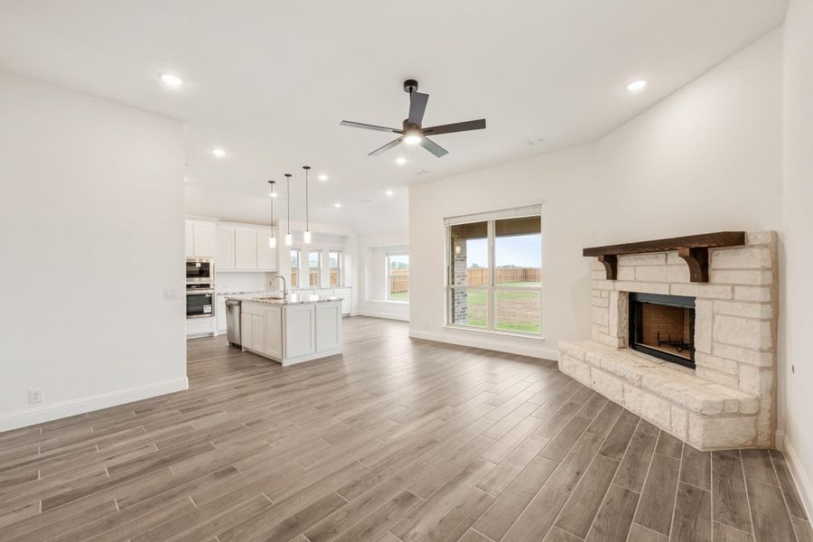 Open living area with stone fireplace, ceiling fan, and kitchen island visible in background