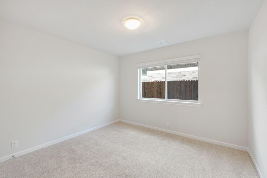 Empty bedroom with beige carpet, white walls, and a single window overlooking a wood fence