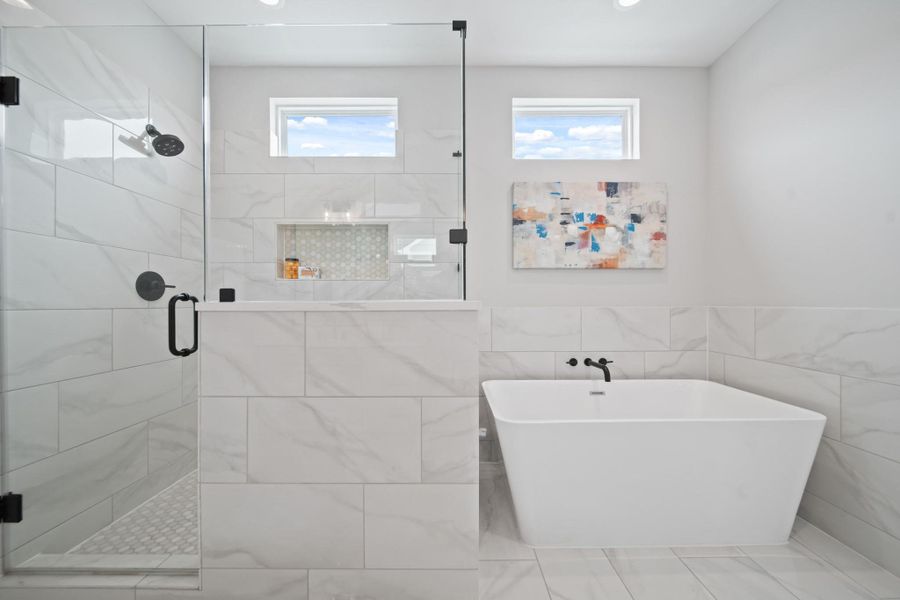 Just beside the freestanding tub, a sleek frameless glass shower offers a quartz bench, hexagon tile flooring and a full tile surround, blending luxury with comfort. A glass framed shower and bold black plumbing fixtures add contrast and style along with a freestanding soaking tub with modern black, wall-mounted fixture. Just beside the freestanding tub, a sleek frameless glass shower offers a quartz bench, hexagon tile flooring and a full tile surround, blending luxury with comfort. A glass framed shower and bold black plumbing fixtures add contrast and style along with a freestanding soaking tub with modern black, wall-mounted fixture.