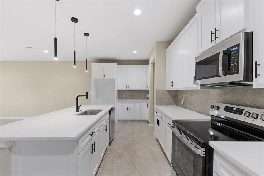 Kitchen with pendant lighting, sink, decorative backsplash, white cabinetry, and stainless steel appliances