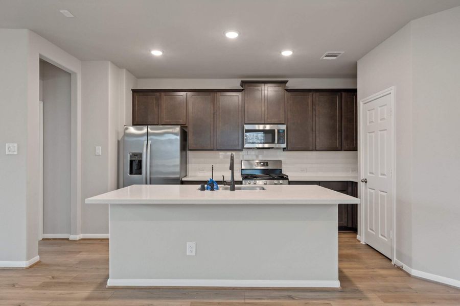 This light and bright kitchen features a large quartz island, dark stained cabinets, a large sink overlooking your family room, recessed lighting, and beautiful backsplash.