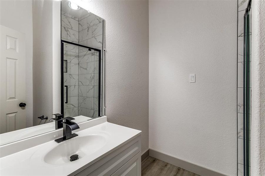 Full bathroom featuring a textured wall, a marble finish shower, vanity, and light wood-style flooring Full bathroom featuring a textured wall, a marble finish shower, vanity, and light wood-style flooring