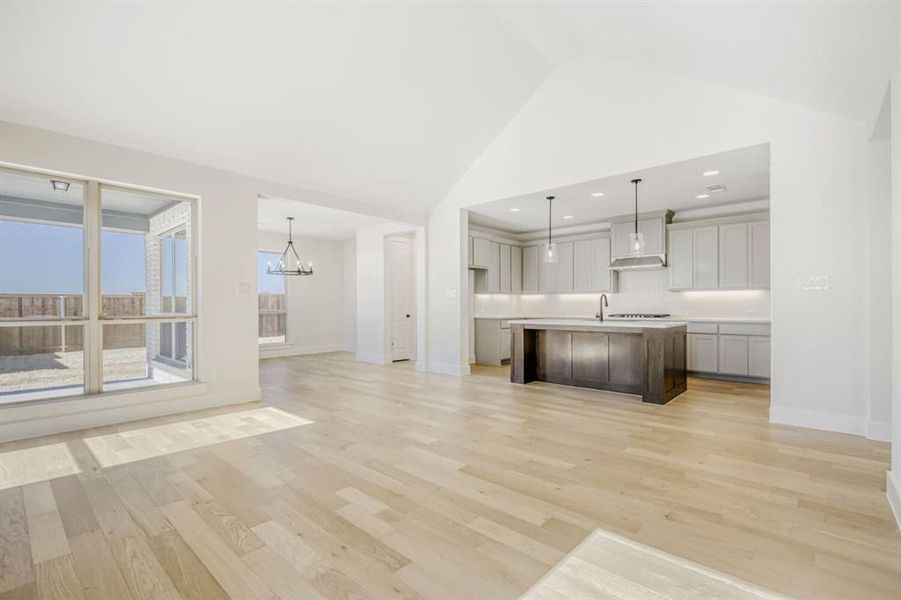 Dual tone kitchen with open floor plan, light countertops, an island with sink, a chandelier, and a high ceiling