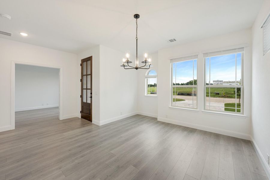 Empty dining room with light hardwood floors, chandelier, large windows, and a wood-framed glass door.
