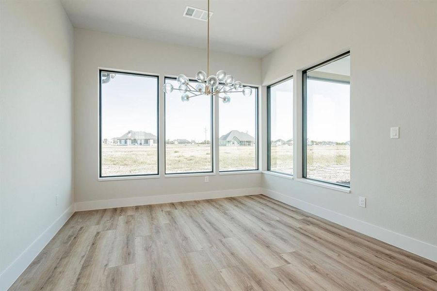 Example of builders Unfurnished dining area featuring light wood-type flooring and an decorative chandelier