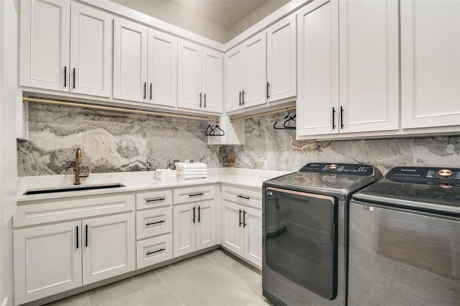 Clothes washing area with sink, cabinets, light tile patterned floors, and washing machine and clothes dryer