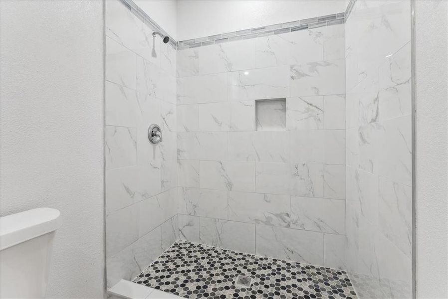 Full bath featuring a textured wall, a tile shower, and toilet