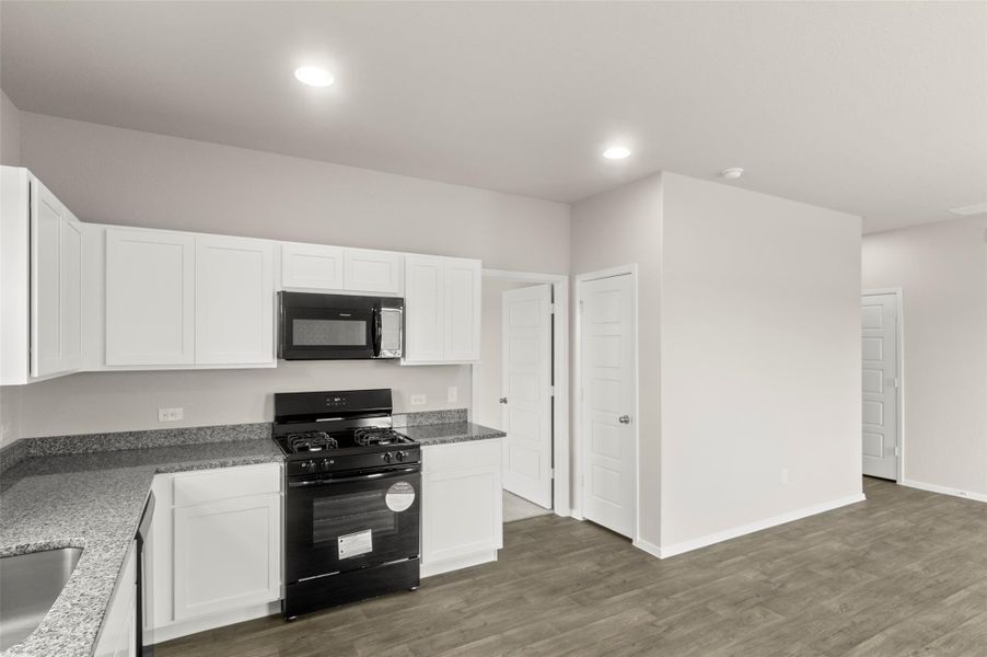 Kitchen featuring black appliances, white cabinetry, wood finished floors, recessed lighting, and stone countertops