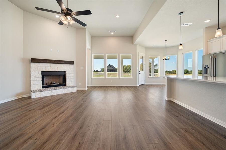 Unfurnished living room featuring a chandelier, a stone fireplace, dark wood finished floors, recessed lighting, and a ceiling fan