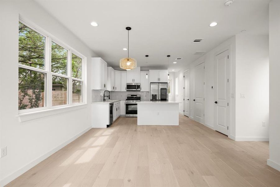 Kitchen featuring a center island, light countertops, white cabinetry, stainless steel appliances, and light wood-style floors