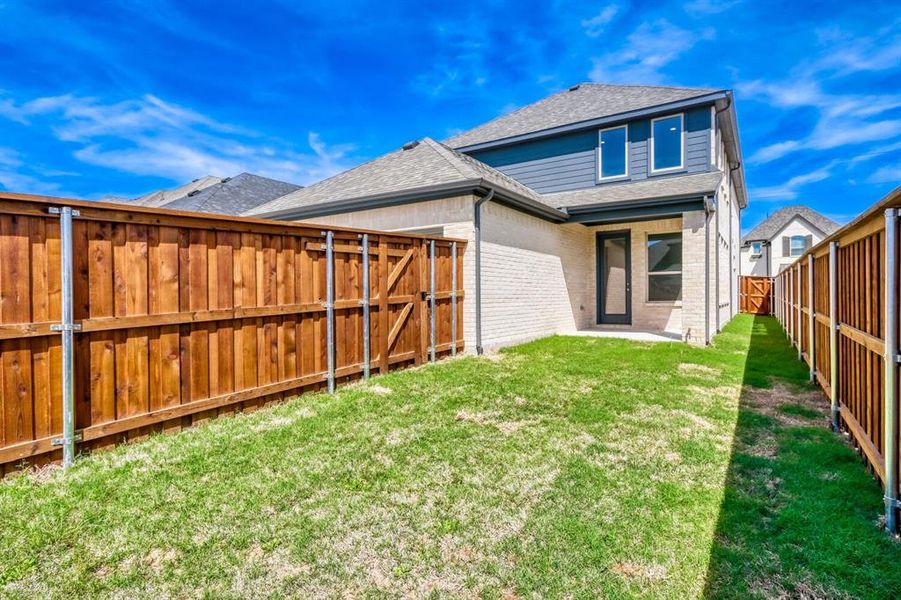 Rear view of property with brick siding, roof with shingles, a fenced backyard, a gate, and a patio
