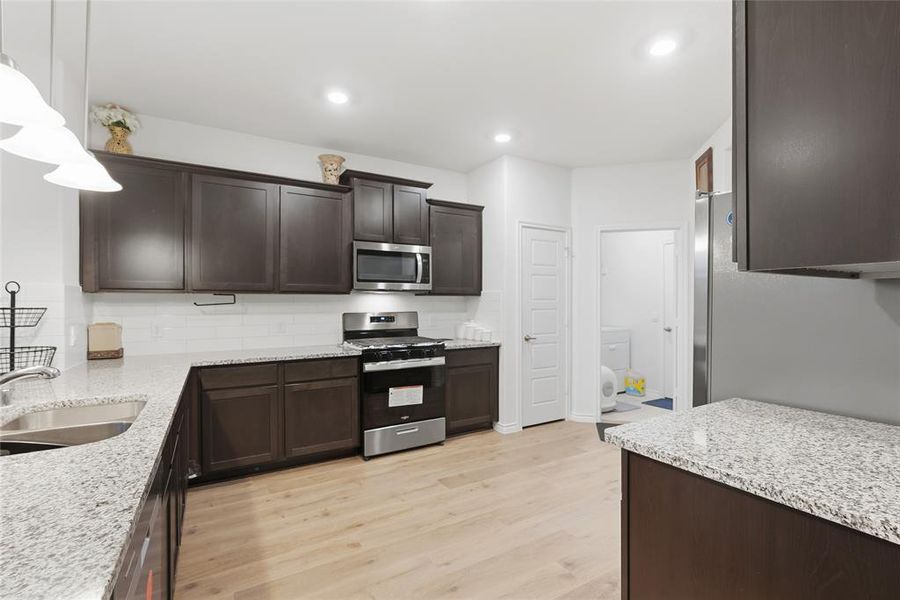 Modern kitchen featuring dark wood-finish cabinetry, light granite-style countertops, stainless steel appliances, white subway tile backsplash, and wood-finish flooring
