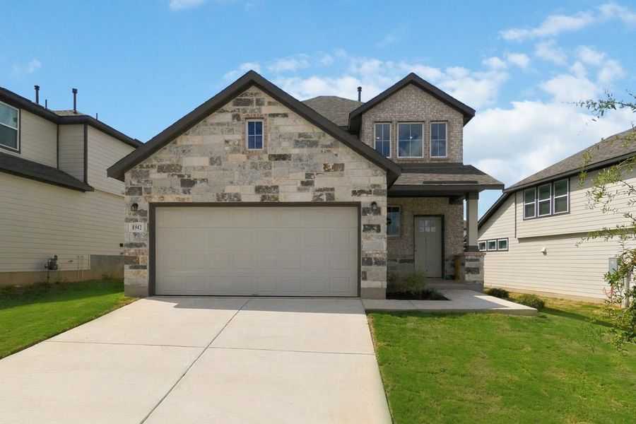 Two-story home with stone exterior, two-car garage, and concrete driveway with green lawn