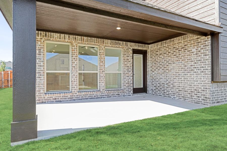 Covered back patio with concrete floor, brick exterior, large windows, and back door entry