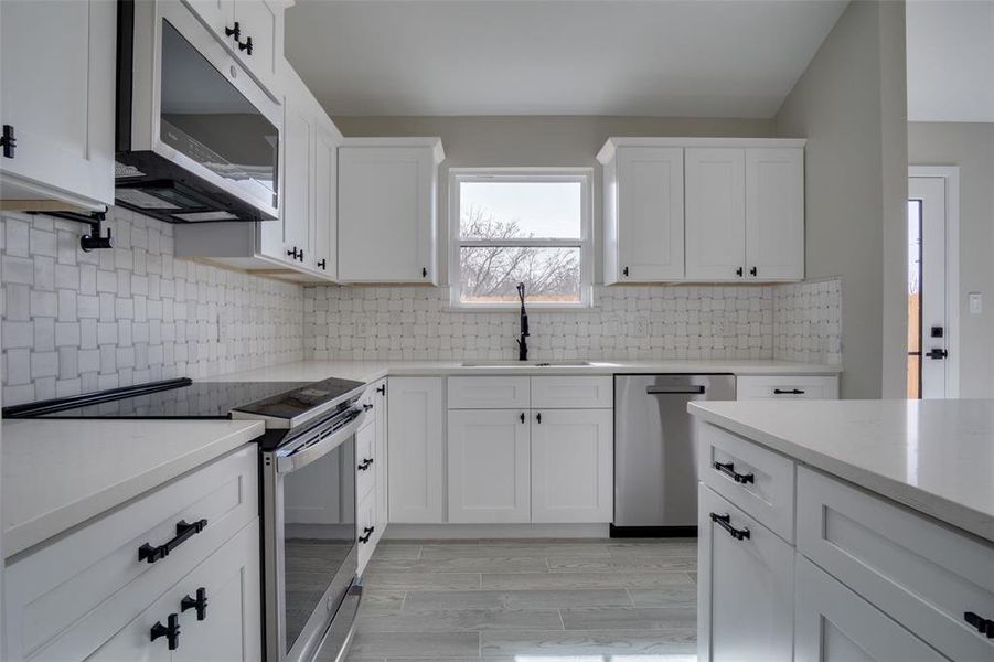 Kitchen with a sink, stainless steel appliances, white cabinets, and light countertops