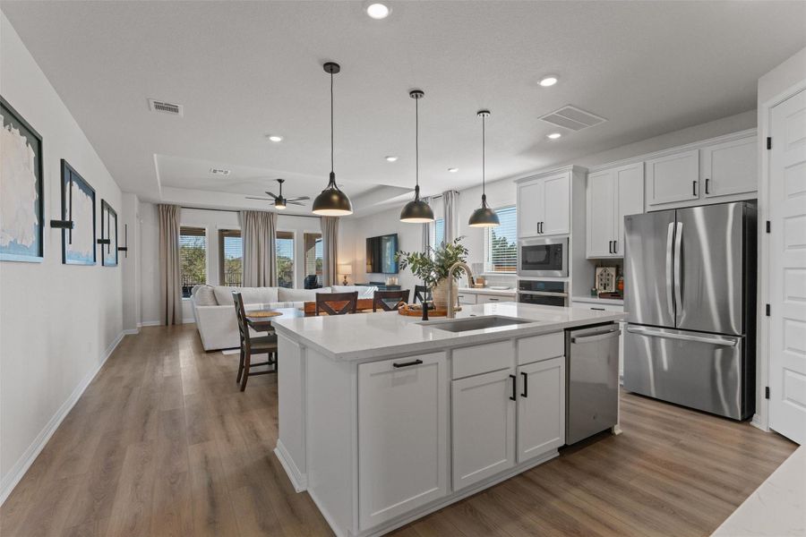 Kitchen featuring stainless steel appliances, white cabinets, decorative light fixtures, open floor plan, and light wood-type flooring