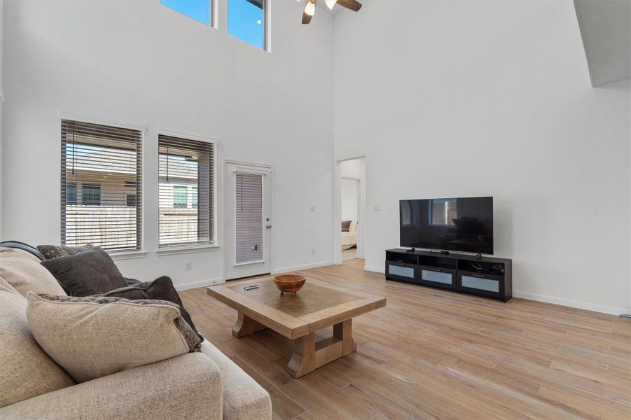 Living room featuring light wood finished floors, ceiling fan, and a high ceiling