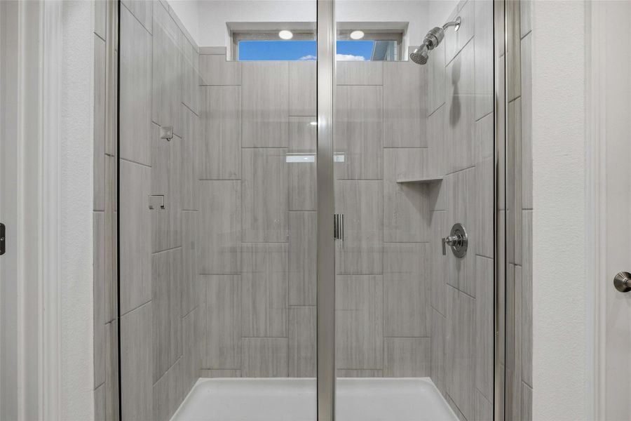 Walk-in shower featuring glass enclosure, light-toned tile walls with varied pattern, recessed storage niche, and chrome fixtures