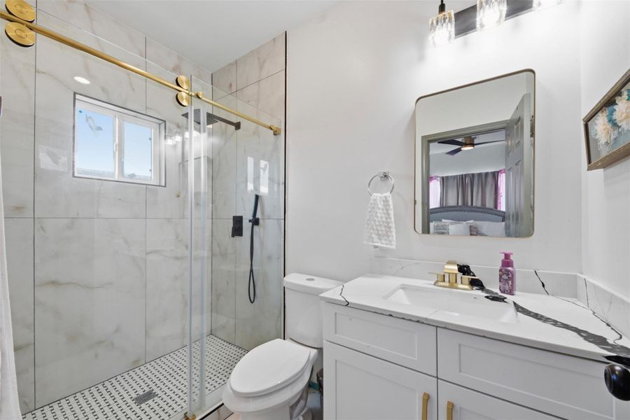 This modern bathroom features a sleek glass-enclosed shower with elegant gold hardware, a stylish vanity with a marble countertop, and contemporary lighting. The space is bright and well-organized, offering a luxurious feel.