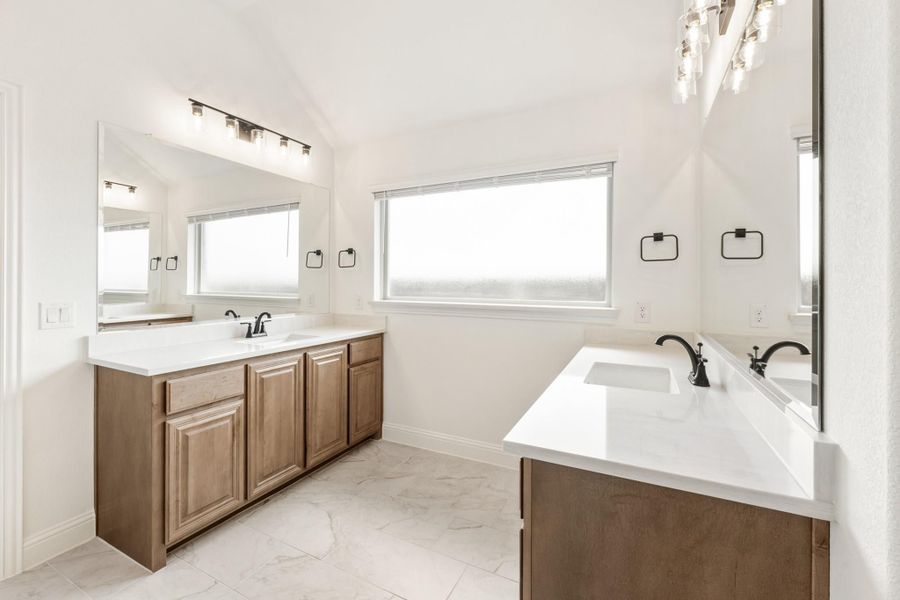 Bathroom with dual vanities, wood cabinets, white countertops, and marble tile floors