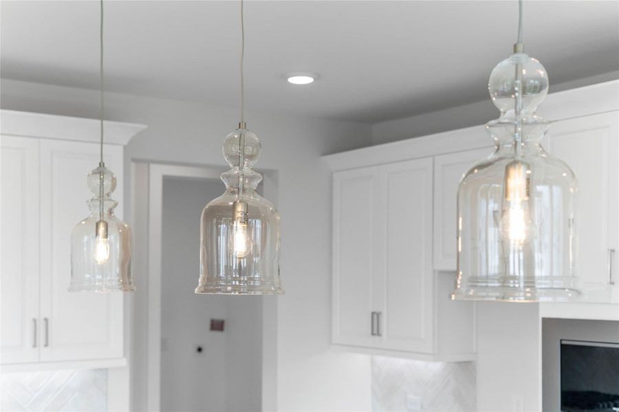 Three exquisite, bell-shaped clear glass pendant lights that elegantly hang above the kitchen island, providing focused task lighting and a touch of refined style.