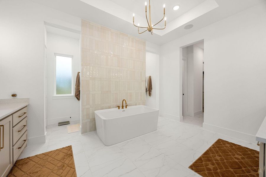 This spacious bathroom features a modern freestanding tub, elegant chandelier, and sleek cabinetry. The room is bright with natural light from a frosted window and has a clean, minimalist design with neutral tones and stylish tile accents.