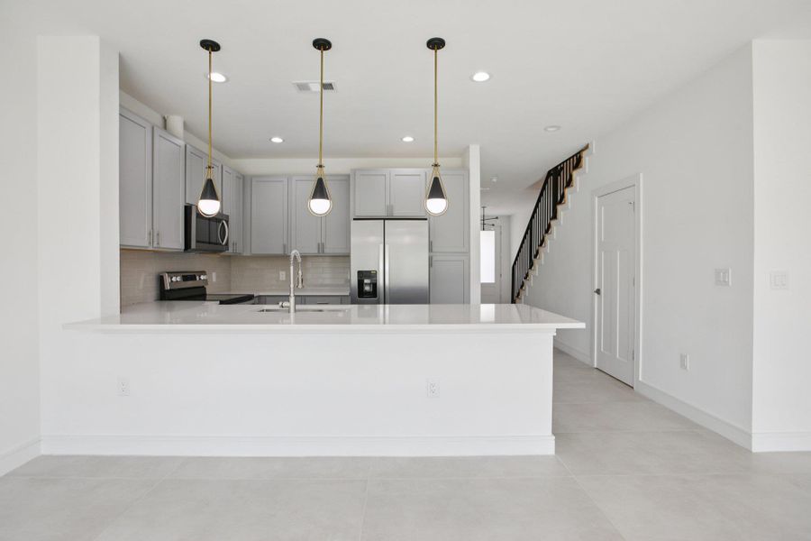 Kitchen featuring gray cabinets, tasteful backsplash, stainless steel appliances, a peninsula, and light stone counters