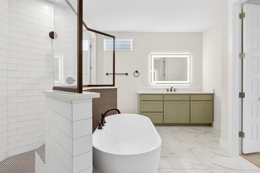 Freestanding soaking tub with dark bronze fixtures, a walk-in shower featuring white subway tile and a dark bronze framed glass enclosure, and a light green vanity with a quartz countertop and an illuminated mirror Freestanding soaking tub with dark bronze fixtures, a walk-in shower featuring white subway tile and a dark bronze framed glass enclosure, and a light green vanity with a quartz countertop and an illuminated mirror