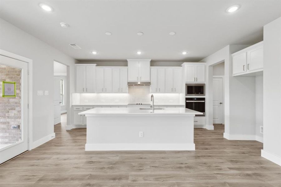 Kitchen featuring black appliances, an island with sink, white cabinetry, light countertops, and recessed lighting Kitchen featuring black appliances, an island with sink, white cabinetry, light countertops, and recessed lighting