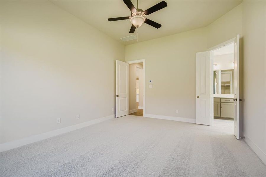 Unfurnished bedroom with light colored carpet, ceiling fan, and ensuite bathroom