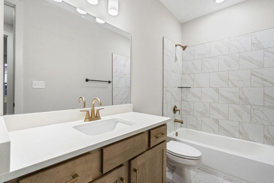 Bathroom with a white countertop vanity, wood-finish cabinetry, and gold-tone fixtures Bathroom with a white countertop vanity, wood-finish cabinetry, and gold-tone fixtures