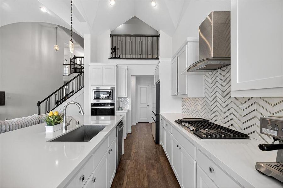 Kitchen with white cabinetry, tasteful backsplash, wall chimney range hood, high vaulted ceiling, and dark wood finished floors Kitchen with white cabinetry, tasteful backsplash, wall chimney range hood, high vaulted ceiling, and dark wood finished floors