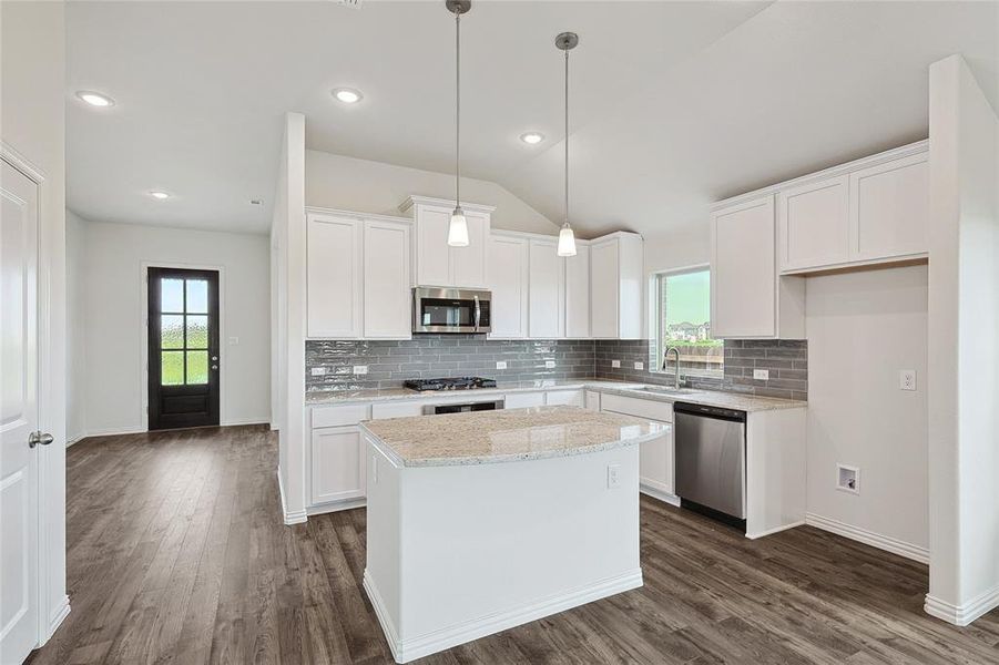 Kitchen featuring appliances with stainless steel finishes, white cabinetry, vaulted ceiling, dark wood-type flooring, and a center island