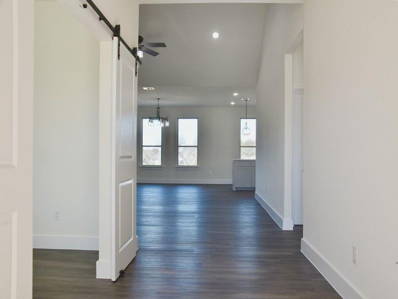 Corridor with a barn door, an inviting chandelier, and dark wood-type flooring