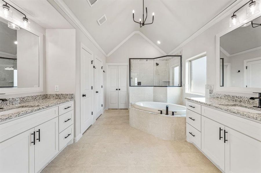 Full bathroom with vaulted ceiling, ornamental molding, a stall shower, a garden tub, and two vanities