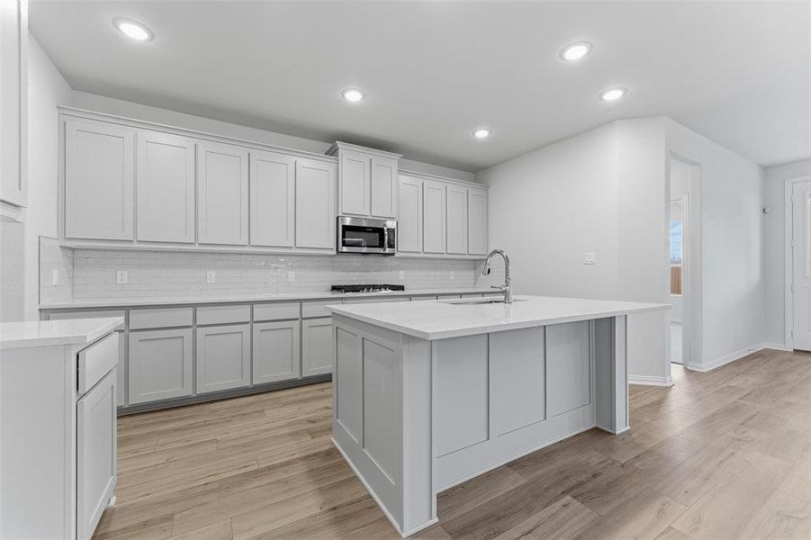 Kitchen with decorative backsplash, an island with sink, light stone counters, recessed lighting, and stainless steel appliances