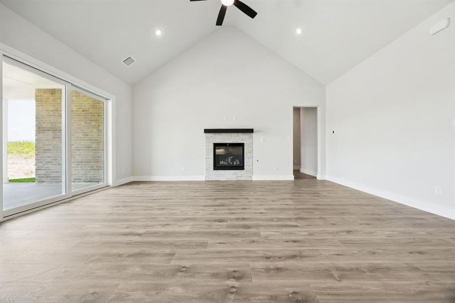 Unfurnished living room with high vaulted ceiling, light wood finished floors, a fireplace, and ceiling fan