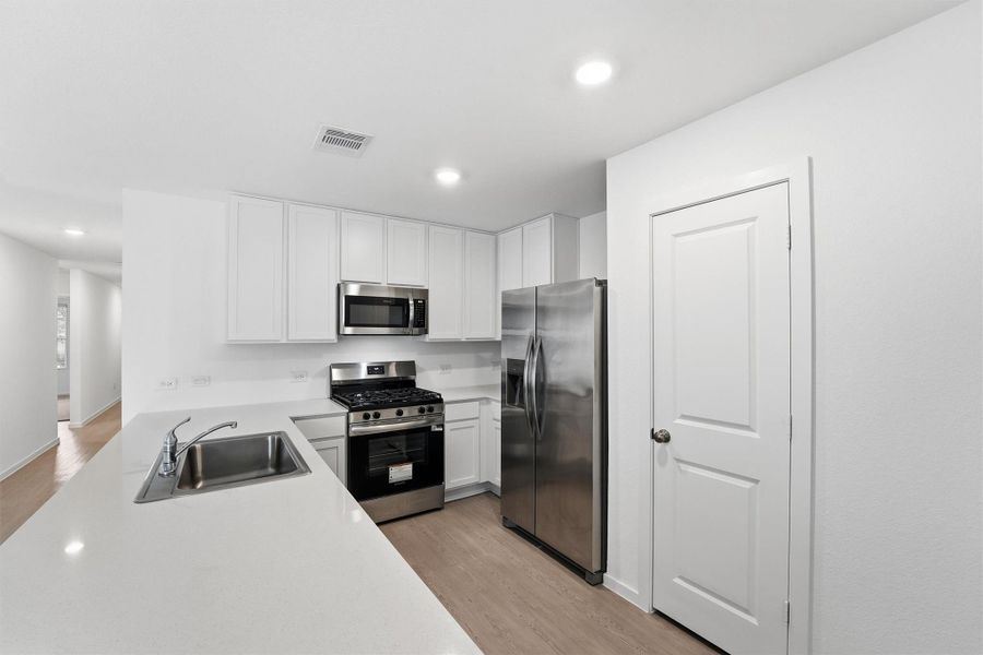 This modern kitchen features sleek stainless steel appliances, white cabinetry, and a spacious countertop with an integrated sink. The open layout and light wood flooring create a bright and inviting space.