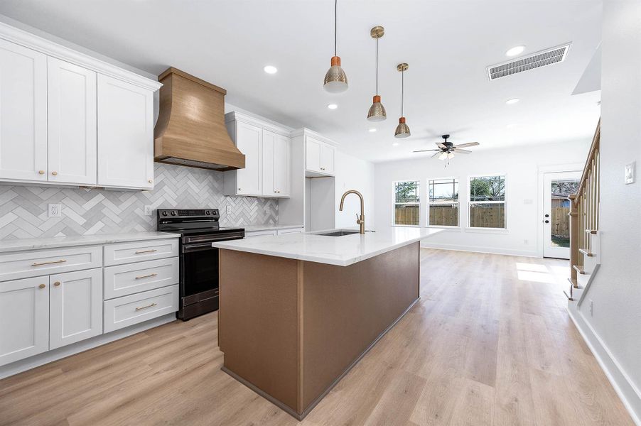 Bright open-concept kitchen featuring a large quartz island, custom wood vent hood, white cabinetry, and stylish pendant lighting overlooking the living area. Bright open-concept kitchen featuring a large quartz island, custom wood vent hood, white cabinetry, and stylish pendant lighting overlooking the living area.