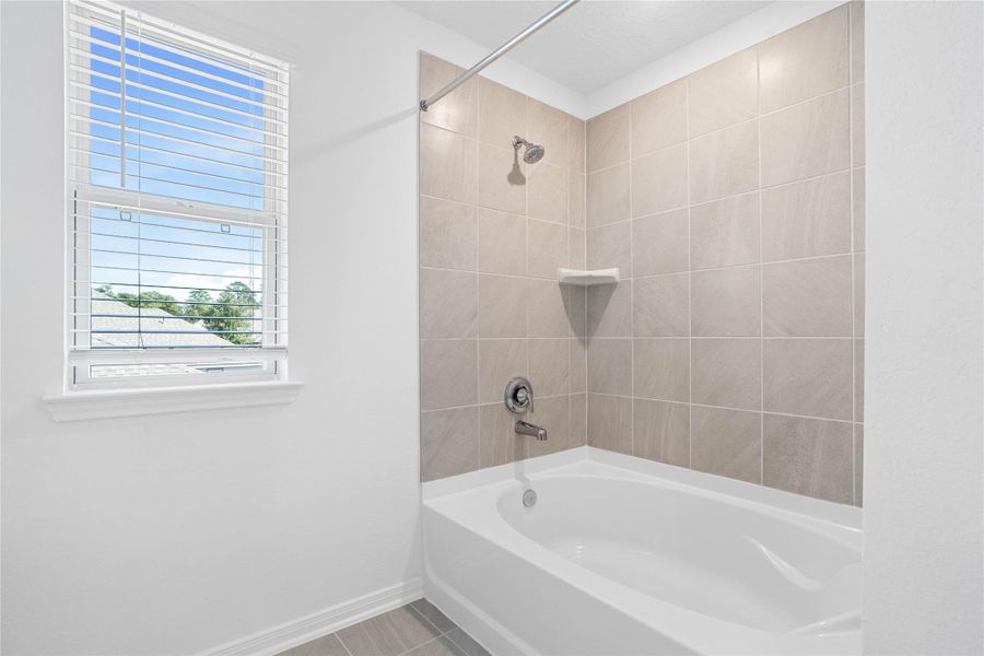This additional view of the primary bath highlights an oversized tub/shower combination with tile surround, and a large window with blinds that offers both natural light and privacy.
