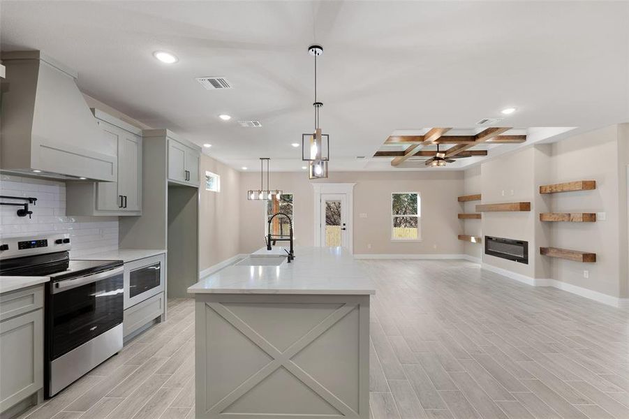 Kitchen with coffered ceiling, backsplash, stainless steel range with electric stovetop, ceiling fan, and custom exhaust hood