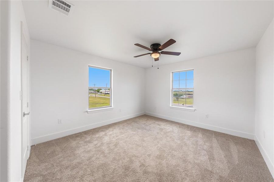 Spacious room featuring neutral carpeting, white walls, two windows, a ceiling fan, and white trim