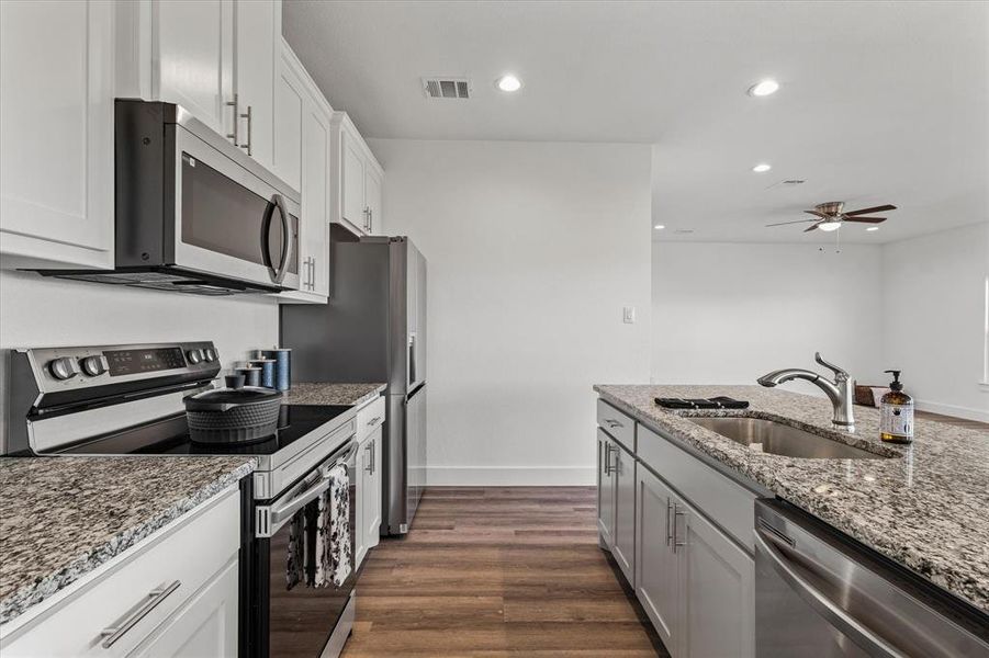Kitchen featuring sink, light stone counters, dark hardwood / wood-style flooring, white cabinets, and appliances with stainless steel finishes