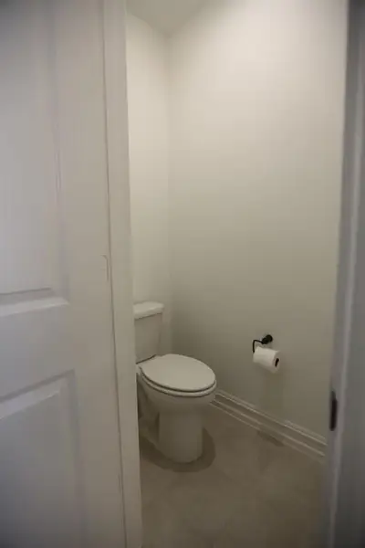 Toilet with tile flooring, white walls, and a black toilet paper holder